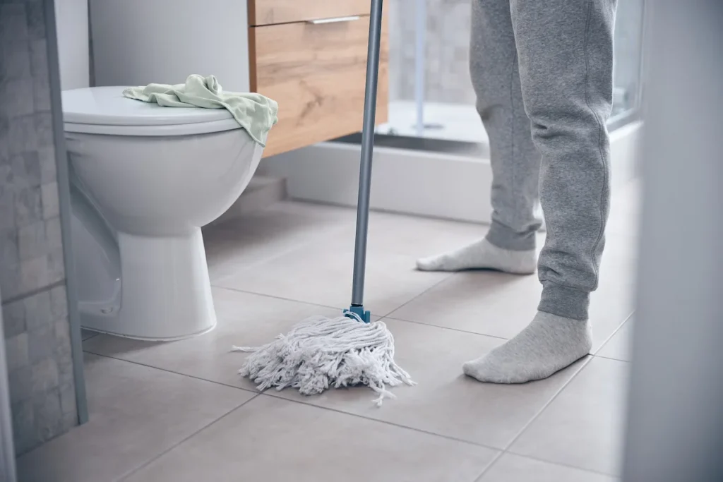 Mop cleaning bathroom floor near toilet in tiled restroom