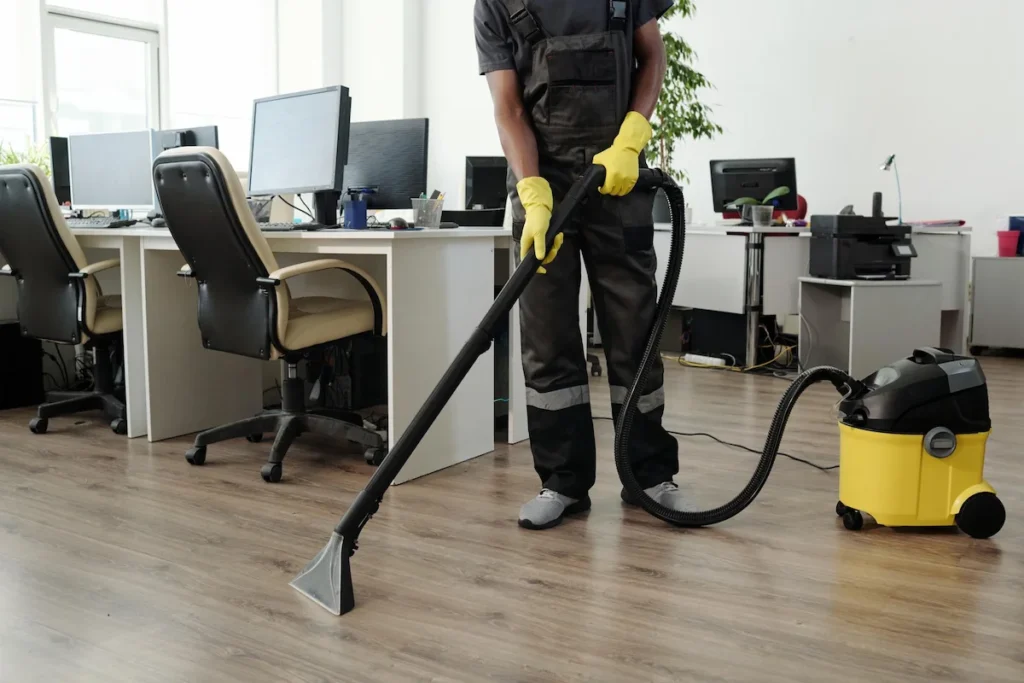 Janitorial staff vacuuming carpet in open office workspace